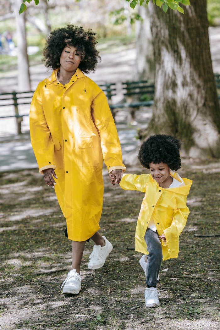 Smiling mother and daughter enjoying a walk in matching yellow raincoats on a sunny day.